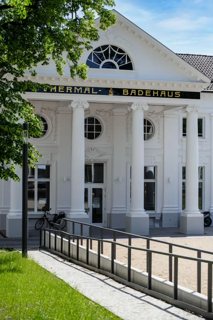 Loepraxis Dr Wilamowskiweb005 Dr Matthias Willamowski Kollegen White neoclassical building with tall columns and a dark sign reading THERMAL BAD EHAUS at the entrance greenery framing the facade