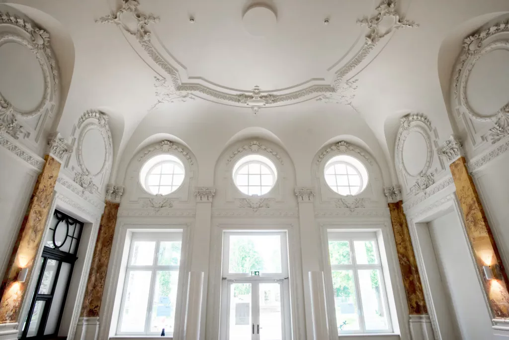 Loepraxis Dr Wilamowskiweb010 Dr Matthias Willamowski Kollegen Elegant white interior with ornate plasterwork circular windows and marble columns framing a glass door entrance