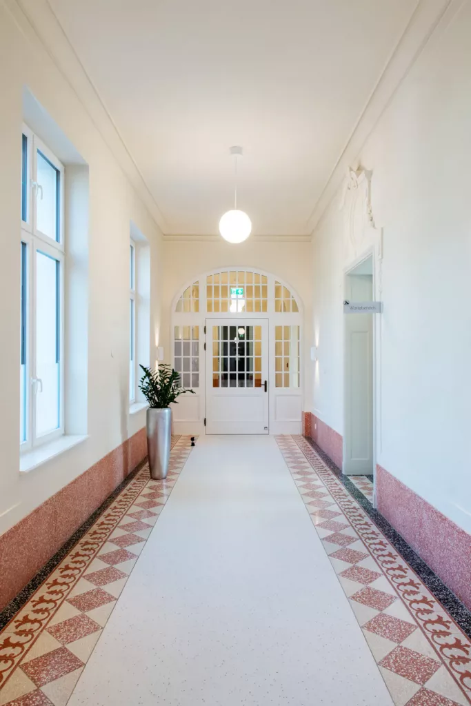 Loepraxis Dr Wilamowskiweb016 Dr Matthias Willamowski Kollegen Bright white hallway with decorative tiled border tall windows and a glass paned double door at the end due to symmetry and light