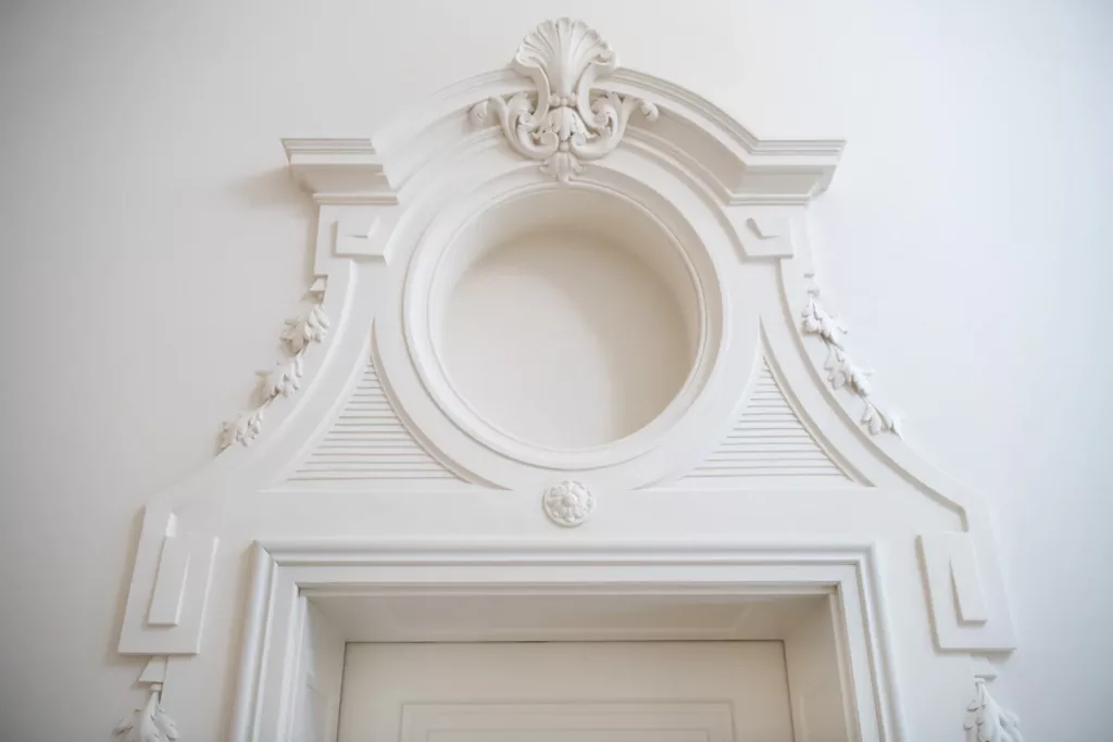 Loepraxis Dr Wilamowskiweb026 Dr Matthias Willamowski Kollegen White ornate door surround with a circular central medallion and decorative scrolling moldings on a pale wall