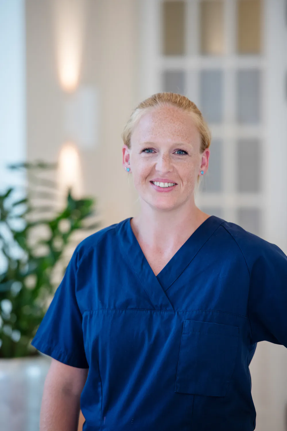 Loepraxis Dr Wilamowskiweb029 Dr Matthias Willamowski Kollegen Smiling female healthcare worker in blue scrubs standing in a bright modern interior
