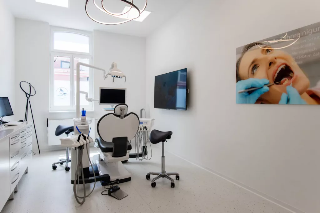 Loepraxis Dr Wilamowskiweb039 Dr Matthias Willamowski Kollegen Modern dental treatment room with a chair overhead light and dental tools a wall mounted monitor and a large poster on the right