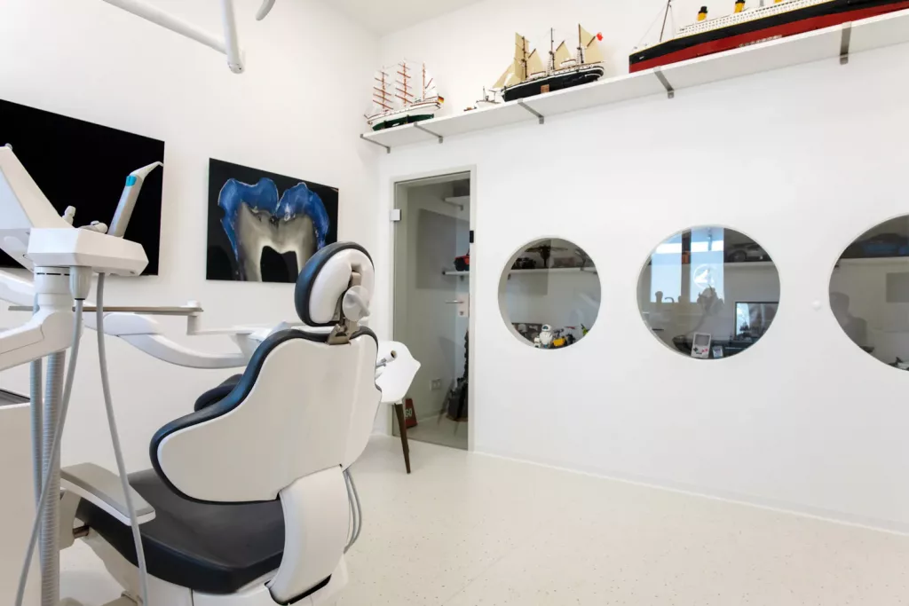 Loepraxis Dr Wilamowskiweb040 Dr Matthias Willamowski Kollegen Modern dental clinic with a white reclining chair overhead equipment and ship models on a shelf above the doorway