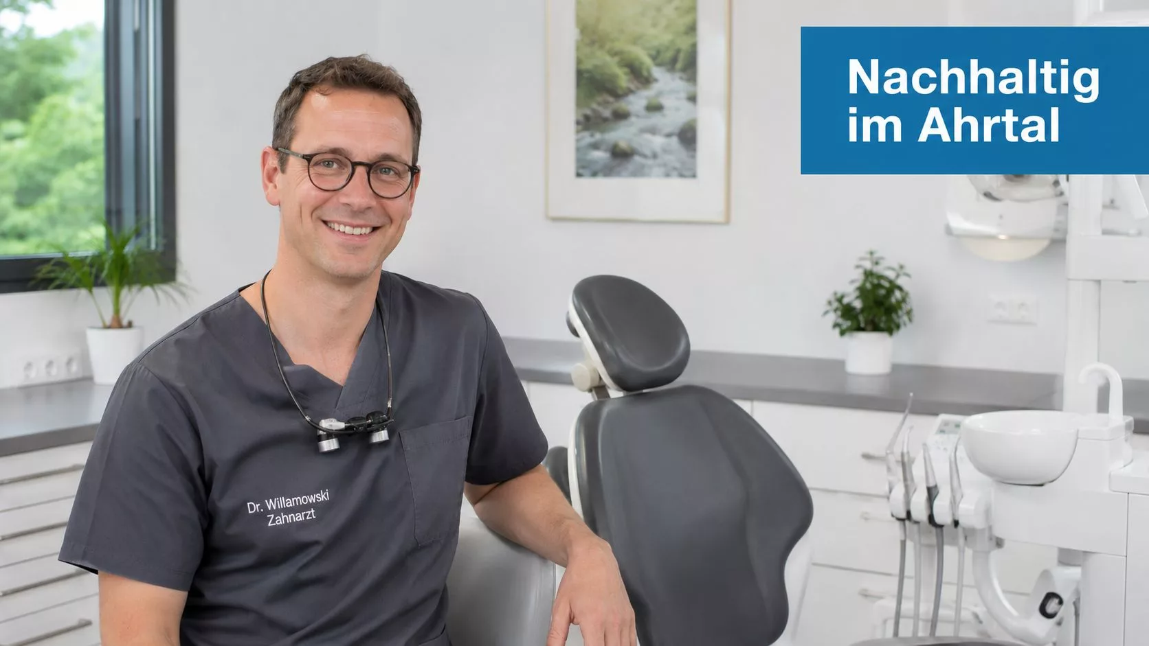 Ein lächelnder Zahnarzt im grauen Kasack sitzt professionell in seiner modernen, hellen Zahnarztpraxis im Ahrtal.